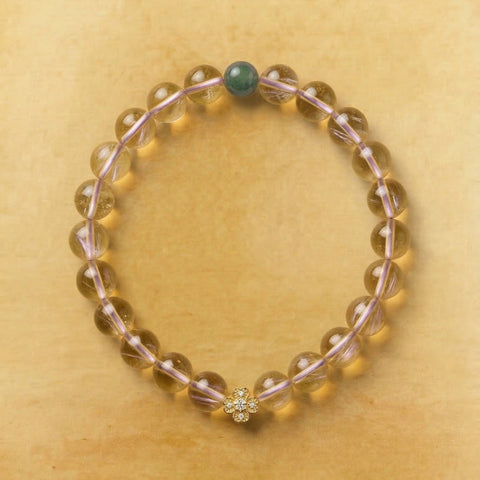 AETHER Key: ABUNDANCE natural citrine bracelet with Burmese jadeite accent and gold floral spacer, translucent golden beads on a warm parchment background.