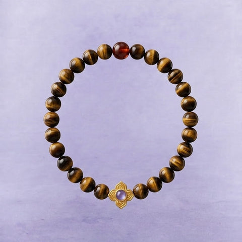 AETHER Key: FOCUS tiger's eye bracelet with orange-red garnet and gold floral pendant, shimmery golden-brown beads on a soft purple textured background.
