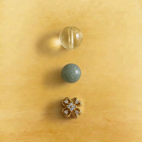 Macro detail of AETHER Key: ABUNDANCE, showing a flawless golden citrine bead, a smooth green Burmese jadeite bead, and a detailed gold floral spacer.