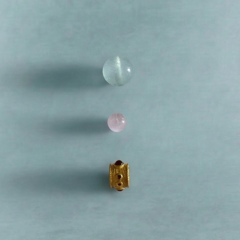 Macro detail of AETHER Key: FLOW, showing a milky aquamarine bead, a cat's-eye kunzite bead, and a detailed gold focal element with ruby-toned inlays.