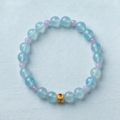 AETHER Key: FLOW milky aquamarine bracelet with lavender kunzite accents and a gold focal bead, soft pastel blue beads on a light blue background.