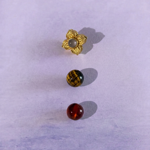 Macro detail of AETHER Key: FOCUS, showing the gold-plated floral pendant with inlay, a chatoyant tiger's eye bead, and a translucent deep red garnet bead.