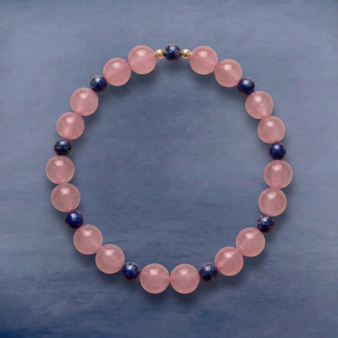 AETHER Key: RESONANCE Madagascar rose quartz bracelet with lapis lazuli accent and gold spacers, translucent pink beads on a cool grey-blue background.
