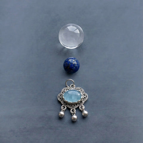 AETHER Energy Alignment - Minimalist vertical arrangement featuring a clear quartz sphere, a natural lapis lazuli bead, and an intricate silver pendant with aquamarine on a dark grey background.